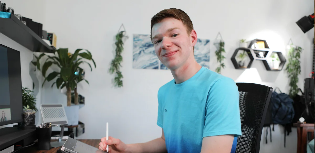 Student wearing a light blue shirt and taking notes at home